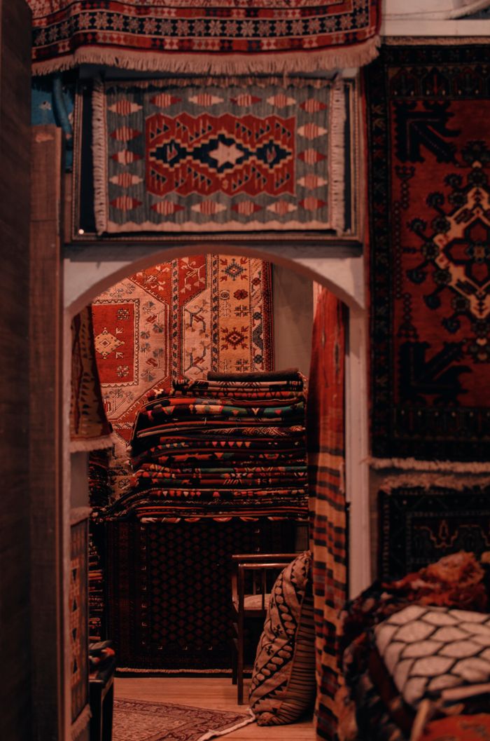 A collection of vibrant, traditional Persian rugs in a dimly-lit artisanal shop interior.